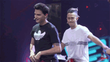 a man in a black adidas shirt stands next to another man in a white shirt