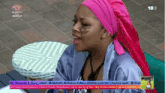 a woman wearing a pink head scarf is sitting at a table in front of a big brother logo