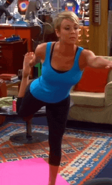 a woman in a blue tank top is doing yoga on a pink mat in a living room