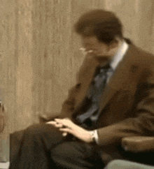 a man in a suit and tie is smoking a cigarette while sitting in a chair