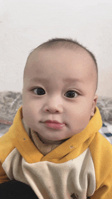 a baby is wearing a yellow and white sweater and looking at the camera