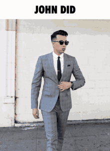 a man in a suit and tie is standing in front of a white wall with the name john did on it