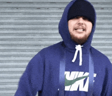 a man wearing a blue nike hoodie stands in front of a metal shutter