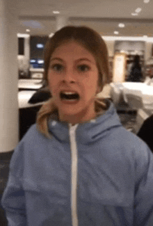 a girl in a blue jacket is making a funny face with her mouth open