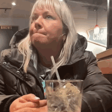 a woman is sitting at a table with a glass of water and a straw in front of a sign that says brews