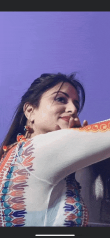 a woman in a colorful dress is standing in front of a purple wall and smiling