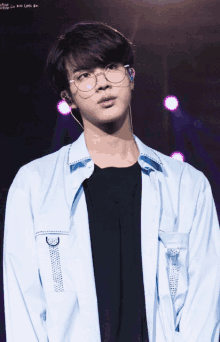 a young man wearing glasses and a blue shirt is standing on a stage