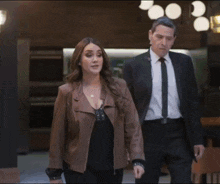 a man in a suit and tie walks next to a woman in a brown jacket