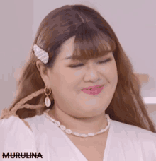 a woman wearing a white shirt and a pearl necklace has the name murulina on the bottom right