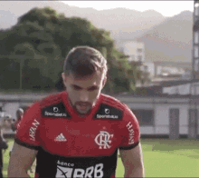 a man is standing on a soccer field wearing a red and black shirt with the word banco on it .