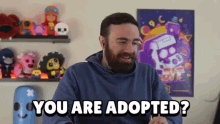 a man with a beard says " you are adopted " in front of a shelf full of stuffed animals