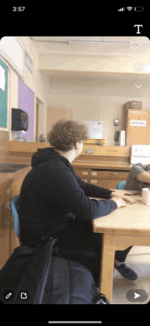 a phone screen shows a person sitting at a table with a sign that says spoons