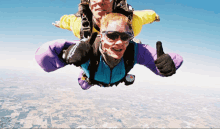 a man wearing sunglasses is giving a thumbs up while flying with another man