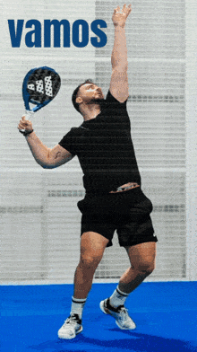 a man in a black shirt is holding a tennis racquet in front of a sign that says " vamos "