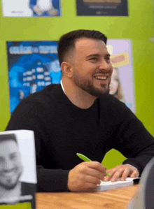 a man with a beard is sitting at a table with a pen in his hand