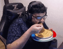 a man wearing headphones is sitting in a chair eating food from a plate .