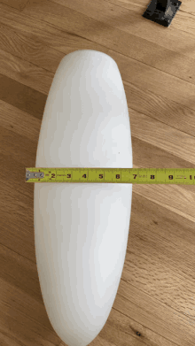 a yellow tape measure measures the length of a white object on a wooden surface