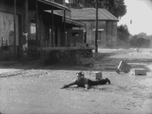 a black and white photo of a man laying on the ground in front of a building with the letter s on it