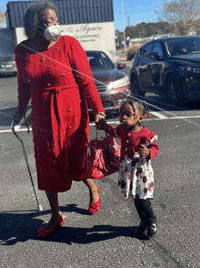 a woman in a red dress is walking with a little girl