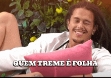 a man with dreadlocks is smiling while holding a pink pillow with the words quem treme e folha written above him