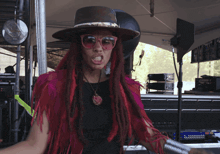 a woman with red dreadlocks wearing a hat and sunglasses is making a funny face
