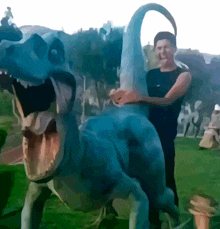 a man is standing next to a blue dinosaur statue