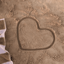 a heart is drawn in the sand next to a towel