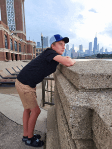 a young man leans on a concrete wall with a city skyline in the background