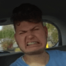 a young man in a blue shirt is making a funny face in a car .