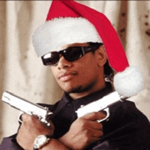 a man wearing sunglasses and a santa hat holds two guns