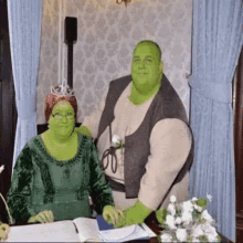 a man and a woman dressed as shrek are sitting at a table with a book .