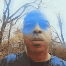 a man with blue paint on his face is standing in front of trees