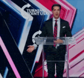 a man in a suit and tie is standing at a podium in front of a turning point usa sign