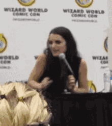 a woman is sitting at a table with a microphone in front of a sign that says wizard world comic con .