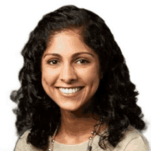 a woman with curly hair and a necklace smiles for the camera .