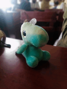 a green stuffed animal is sitting on a table in a classroom