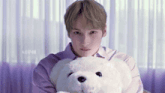 a young man in a purple shirt holds a white teddy bear .