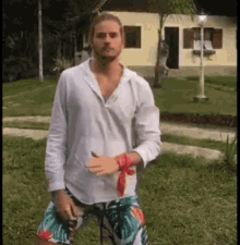 a man in a white shirt and colorful shorts is standing in front of a house in a yard .