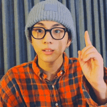 a man wearing glasses and a plaid shirt points up