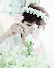 a young man with a flower crown on his head is holding a bouquet of flowers .