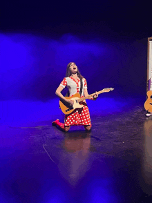 a woman in a red and white polka dot dress is kneeling down playing a guitar