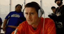 a man wearing headphones and an orange shirt is looking at something