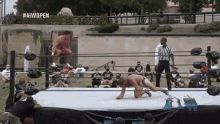 a man is kneeling down in a wrestling ring with a referee in front of a sign that says aiwopen .