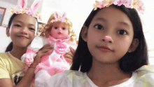 two little girls with bunny ears on their heads holding a doll