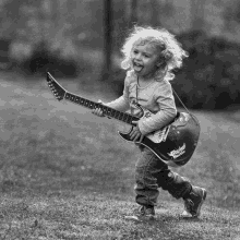 a little girl is playing an electric guitar in the grass in a black and white photo .