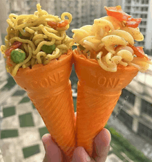 two orange ice cream cones with noodles and vegetables in them