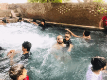 a group of men are swimming in a pool with a brick wall in the background