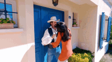 a man in a cowboy hat is standing next to a woman in an orange shirt in front of a blue door .