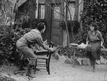 a black and white photo of a man sitting on a chair talking to a woman sitting on a bench