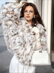 a woman wearing a fur coat and gloves is holding a white purse